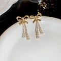 Detail von goldenen Schleifen-Quastenohrringen mit klaren Kristallen und weißen Perlen - Schleife Perle Quaste Stil / Gold/Weiß