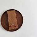 Detail of ginger rib-knit scarf with pink bow and red pompom on wooden tray - Camel