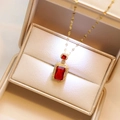 Elegant gold necklace with red rectangular gemstone pendant in a beige jewelry box - Red Necklace