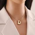 Détail d'un collier avec pendentif lettre D plaqué or 18 carats porté par un mannequin - Lettre D
