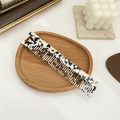 Macro view of wide-tooth tortoiseshell acetate hair comb on a wooden tray with a hanging hole - Black & White