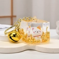 Macro shot of liquid-filled acrylic lucky cat keychain cube with golden bell and beads - Maneki Neko - Gold Ingot
