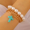 Detail of layered gold link chains with turquoise cross pendant and pearl bracelet - Gold-Cross
