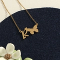 Gold stainless steel initial R necklace with butterfly detail on a textured display - Gold R