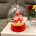 Pallina di Natale luminosa con casetta rossa e albero sopra un libro bianco - Casa Rossa