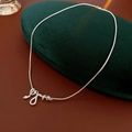 Primer plano de un collar con colgante de serpiente plateado sobre terciopelo verde oscuro - Plateado