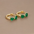 Macro shot of gold bow earrings with two teardrop emerald green zircons on a brown surface - Gold-Green