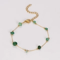 Dettaglio di bracciale a catena dorata con perline di smeraldo verde e chiusura a moschettone - Bracciale