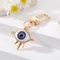Close-up of golden Evil Eye keychain with blue iris, resin insert and sparkling crystals - Rhinestone Purple Eye