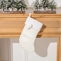 White knitted Christmas stocking with faux fur cuff and pom-poms on wooden fireplace - White