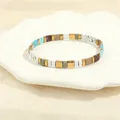 Close-up of bohemian TILA bead stretch bracelet with colorful square enamel tiles - Blue Brown Beige White Marble Gold