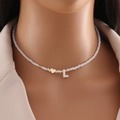 White beaded necklace with gold heart and letter L pendant on a model with beige blazer - L