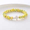 Detail of yellow and green spotted stone beads with a white cross charm on a tray - Yellow Green Spotted White Cross Bracelet