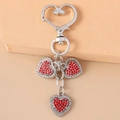 Close-up of heart keychain with red rhinestones and angel wing charms on silver metal - Red