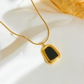 Detailed view of a gold necklace with black rectangular pendant on white silk fabric - Black Shell Necklace