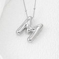 Macro shot of 3D balloon letter M pendant in polished silver on a textured stone surface - Letter M Pendant