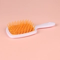 Hollow-out square hairbrush in white handle and orange teeth on pink background - White Handle + Orange