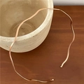 Sleek wave-shaped rose gold metal headband resting on a rustic ceramic jar - Large Wave Wide / Gold