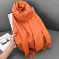 Solid orange faux cashmere scarf with tassels shown against a modern grey sofa - 68x180cm / Orange