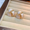 Macro detail of gold-plated knot earrings with pearl white enamel inlay on wooden box - Pearl White