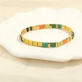 Detailed shot of multi-color Tila bead stretch bracelet in a decorative white shell dish - Yellow Green Orange Black Gold