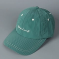 Close-up of green checkered fabric and white Magical secrets embroidery on the baseball cap - Teal