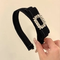 Détail d'un serre-tête en velours noir avec boucle en strass tenu à la main - Noir