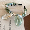Dettaglio del cerchietto in raso verde floreale con denti antiscivolo su libro vintage - Cerchietto Avvolto con Fiocco / Verde