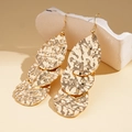 Detail of golden teardrop drop earrings with hammered metal texture on stone stand - Gold
