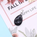 Polished black obsidian teardrop stone pendant with silver clasp on decorative background - Black Agate