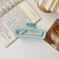Close-up of a matte light blue oversized hollow rectangular hair claw on an open book - Matte Large Square Sky Blue