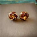 Vista macro de pendientes de nudo de amor vintage con esmalte oscuro y dorado - café