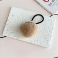 Close-up of soft khaki faux fur pompom hair tie on a white textured plaster board - Khaki