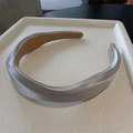 Detalle de diadema plateada trenzada con textura metálica sobre una bandeja blanca - Gris