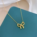 Macro-opname van een gouden strikhanger aan een fijne ketting op donkere textuur - Gouden Ketting
