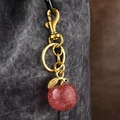 Sparkly red apple keychain with gold clasp on a dark denim texture background - Pink