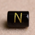 Detailed macro shot of a black cylindrical bead with a gold letter N for DIY jewelry - Letter N