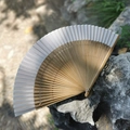 Japanese style bamboo folding fan with light gray fabric placed on a natural rock surface - White