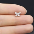 Macro di un piccolo orecchino a farfalla con zirconi trasparenti su una punta di dito - Farfalla in Zircone Argento