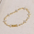 Vue détaillée d'un bracelet trèfle doré avec des fleurs en zircon sur tissu - Fleur Blanche-Or