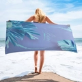 Detail view of microfiber beach towel with purple tropical leaves and Botany text on sand - Purple Tropical Leaves