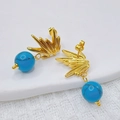 Orecchini ad ala dorati con perline marmorizzate blu su sfondo di tessuto bianco - Stile Turchese Ali / Turchese