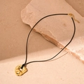 Détail d'un pendentif géométrique doré irrégulier sur cordon noir sur fond de pierre - Pendentif Géométrique Doré / Doré