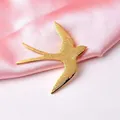 Dettaglio della spilla a forma di rondine dorata con texture fine su seta rosa - Oro Opaco