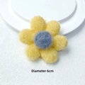 Detail einer 6 cm großen gelben Plüschblume mit dunkelblauem Kern auf weißem Sockel - Brosche Stil / Gelb