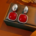 Dettaglio di orecchini quadrati smaltati rossi con elementi argento su pelle bruna - Argento-Rosso