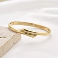 Polished gold geometric stainless steel hollow bangle displayed on a natural stone base - Cross Wrap Style (Style 4)