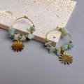 Detail of golden hoop earrings with light green stones and a daisy flower charm - Daisy