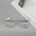 Close-up of clear cat-eye glasses frame with gold metal temples on a desk setting - Clear White