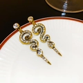 Detail showing golden snake-shaped C-earrings with sparkling white rhinestones - Pave Snake Drop Style / Gold
